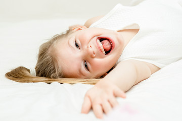 Pretty little blonde girl summer white dress lying on the floor and smiling at camera on white background.