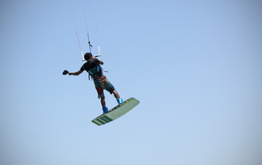 Kite boarding sportsman flying high with kite and kiteboard in boots in the blue sky, active sports and life style, recreation hobby and fun, rider man isolated on the simple air background