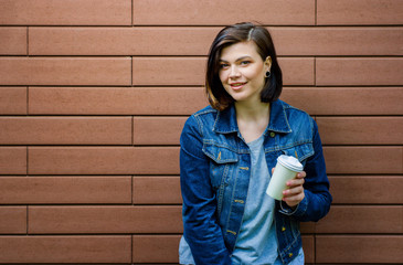 Cheerful girl with a cup of coffee near a brick wall