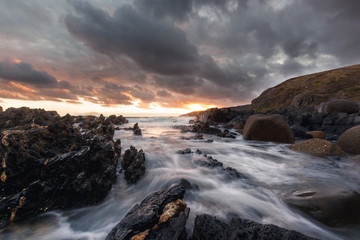 Water crashing over rocks at sunset with dramatic clouds