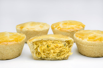 Five traditional Brazilian mini chicken pies called empadas in white background with one cut in the middle close