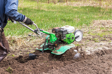 A man works in the garden with the help of a motoblock. Loosening the soil with a cultivator