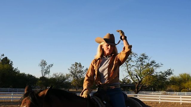 An attractive mature woman puts on her hat while horseback riding