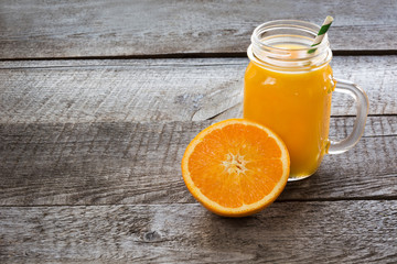 Smoothie of orange in a glass mason jar with slice orange on the old wooden background.