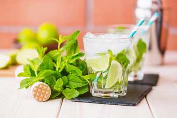 Two fresh mojitos cocktail in glass on wooden table. Mojitos with mint leaves, lime and ice. Drink making tools and ingredients for cocktail.