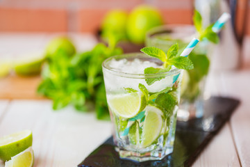 Two fresh mojitos cocktail in glass on wooden table. Mojitos with mint leaves, lime and ice. Drink making tools and ingredients for cocktail.