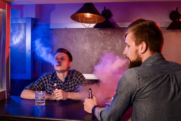 Two young men smoke electronic cigarettes in a vapebar