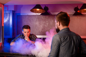 Two young men smoke electronic cigarettes in a vapebar