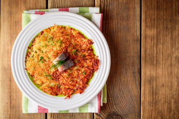 Potato rosti with dill and salted herring in plate on wooden table.