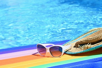 Sunglasses, lilo and hat on the water in hot sunny day. Summer background for traveling and vacation. Holiday idyllic.