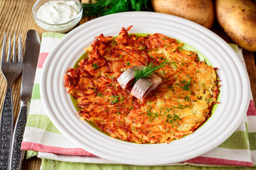 Potato rosti with dill and salted herring in plate on wooden table.