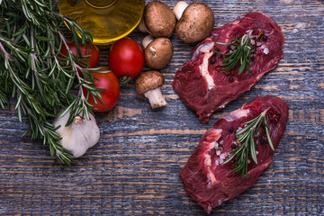 Raw Beef Steak, salt, pepper, garlic, rosemary, olive oil  on the black board, background.
