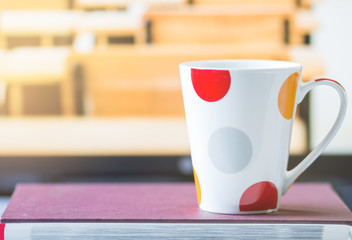 White and red cup coffee on book,  blur desk classroom background, pastel tone