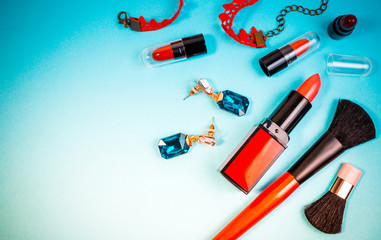 Various makeup cosmetics, brushes, necklace and other essentials on blue background top view. Beauty cosmetics for background concept.