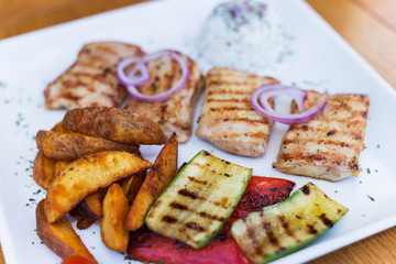 Grilled chicken with grilled vegetables on white plate.