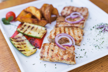 Grilled chicken with grilled vegetables on white plate.