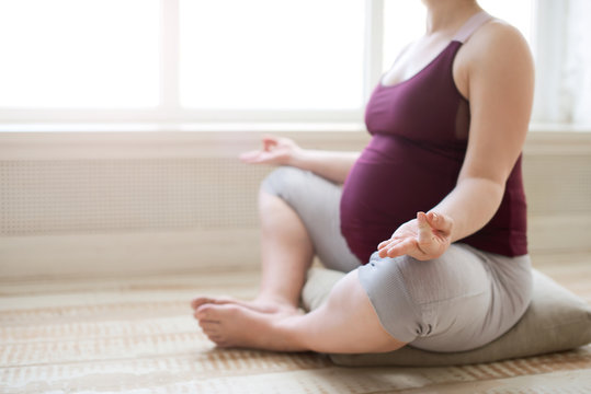 Pregnant woman meditation in lotus pose at home while doing yoga