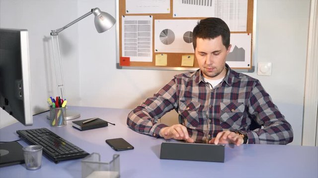 Office worker checks incoming mail on the tablet in his personal account sits at the table in his office. The man uses a touch screen to connect to the Internet.