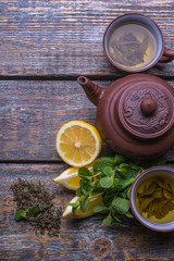 Green Tea cup, tea pot and slices of lemon, ginger, mint, on wooden background