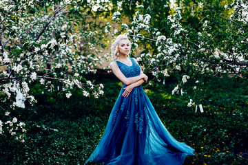 Beautiful young girl in a long evening blue dress in an apple blossoming garden