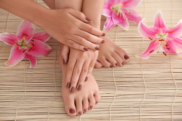 Obraz na płótnie Canvas Female feet and hands with brown manicure on bamboo mat background