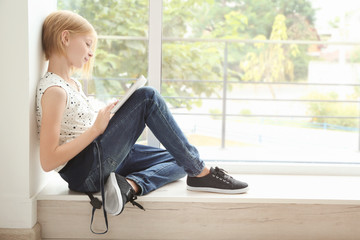 Cute teenager girl with tablet sitting near window