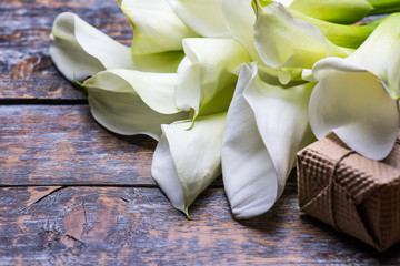 Calla lilies flowers, present box and flowers roses on wooden background