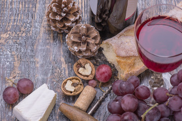 Red wine in a bottle, glass, cork, bottle screw and a set of products - cheese, grapes, nuts, olives, figs on a wooden board, background