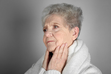 Senior ill woman with sore throat on grey background. Concept of allergy