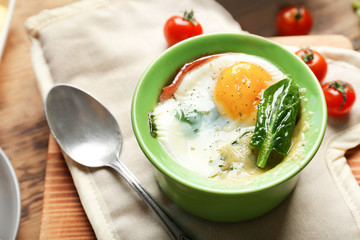 Portion of baked eggs Florentine on wooden kitchen table