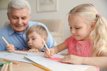 Fototapeta premium Cute little girl painting together with her brother and grandfather