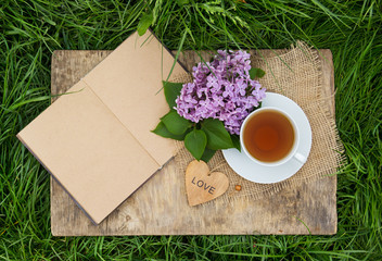 A cup of black tea and an open diary with blank pages on green grass. Romantic concept. Wooden card with a heart. Copy space