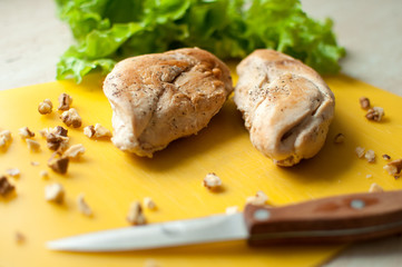 Ruddy chicken breasts with leaf salad and crushed walnut on yellow cutting board.
