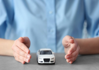Travel insurance concept. Toy car on table and female hands in gesture of protection