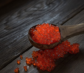 Red caviar in spoon on aged wooden background