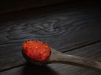 Red caviar in spoon on aged wooden background