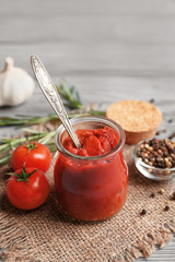 Delicious tomato paste in jar with ingredients on wooden background, closeup