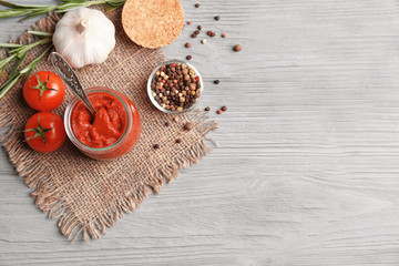 Delicious tomato paste in jar with ingredients on wooden background, top view
