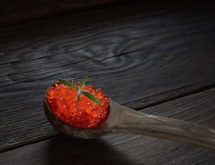 Red caviar in spoon on aged wooden background