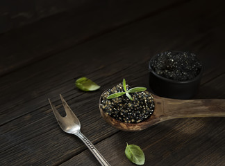 Black caviar in a wooden spoon on a wooden background