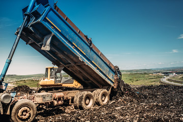 Fototapeta premium industrial dumper trucks unloading garbage into trash hill
