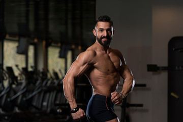 Obraz na płótnie Canvas Handsome Muscular Man Flexing Muscles In Gym