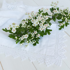 Hawthorn blossom on lace with white wooden background