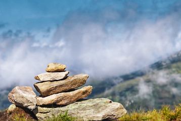 Concept of balance and harmony. Rocks on summit of mountain against valley and clouds.