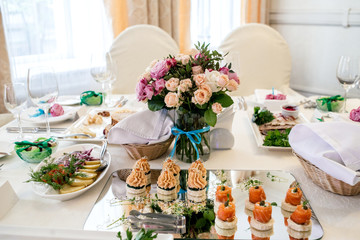 Beautiful wedding bouquet of cream and pink roses in glass vase on dinner table, selective focus. Table setting at a luxury wedding reception. Flowers on the table