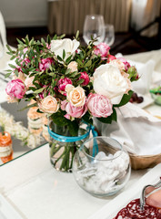 Beautiful wedding bouquet of cream and pink roses in glass vase on dinner table, selective focus. Table setting at a luxury wedding reception. Flowers on the table