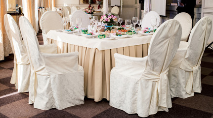 Chairs with white cloth and table for guests served for wedding banquet with flowers. Dinner table for wedding banquet