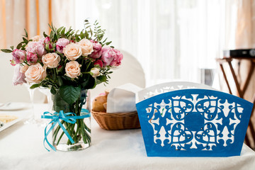 Beautiful wedding bouquet of cream and pink roses in glass vase on dinner table next to blue box for money, selective focus. Flowers on the table