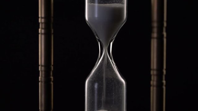 Time Lapse of Sand Flowing Through vintage metal hourglass on black background.