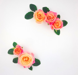 Frame made of pink-orange roses and green leaves on white background. Flat lay, top view